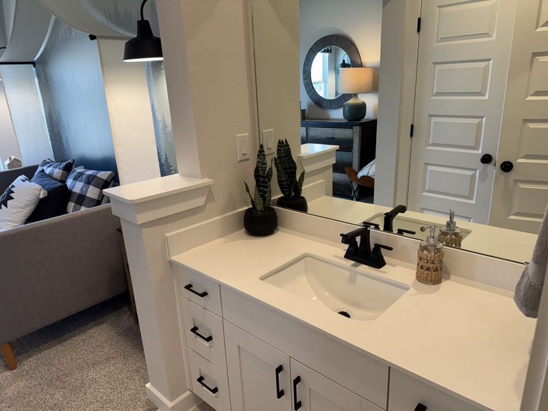 A modern bathroom vanity with a white countertop, black fixtures, and a sleek mirror, adjacent to a cozy living area.
