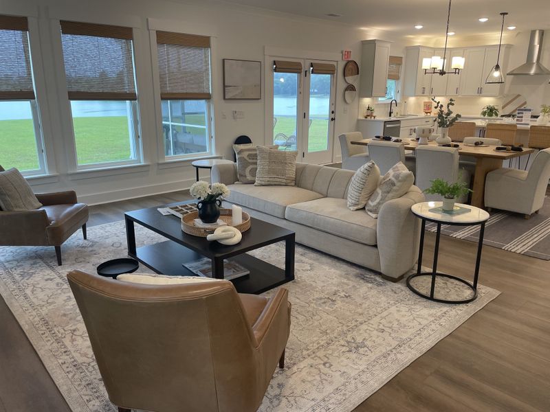 A cozy living area with a beige sofa, soft rug, and elegant dining space overlooking a serene view through large windows.