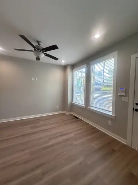 A bright room features sleek hardwood floors, a modern ceiling fan, and large windows inviting ample natural light.