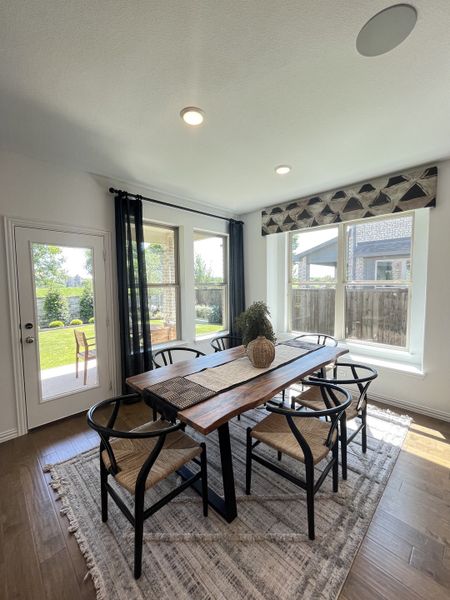 A bright dining area with a wooden table, black chairs, and large windows overlooking a lush backyard.