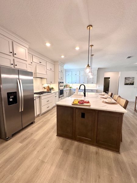 A modern kitchen featuring sleek white cabinetry, a central island with elegant pendant lighting, and stainless steel appliances.