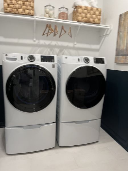 A modern laundry room featuring sleek appliances, wall shelving, and stylish storage baskets. A modern laundry room featuring sleek appliances, wall shelving, and stylish storage baskets.
