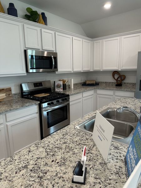 A modern kitchen features sleek granite countertops, white cabinetry, stainless steel appliances, and stylish decor accents. A modern kitchen features sleek granite countertops, white cabinetry, stainless steel appliances, and stylish decor accents.