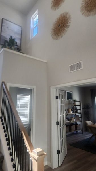 A modern living space with high ceilings, stylish wall decor, and natural light, featuring an elegant staircase and a cozy office nook.