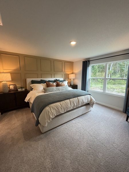 A cozy bedroom featuring a plush bed, soft carpet, and a large window with a view of nature.