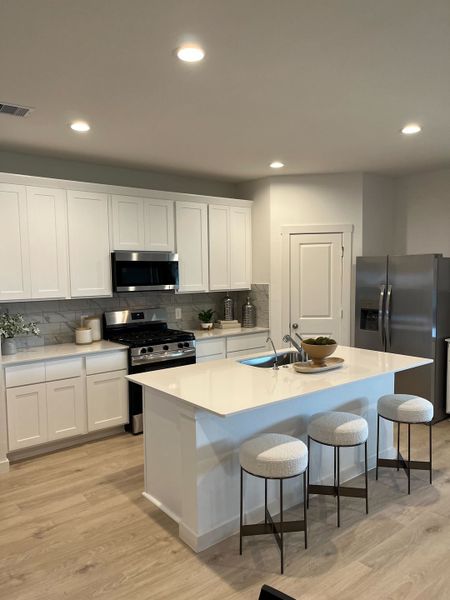Modern kitchen with sleek white cabinets, stainless steel appliances, and a spacious island with stylish stools.