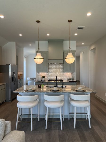 A modern kitchen featuring a sleek island with elegant lighting, marble countertops, and cozy barstools.