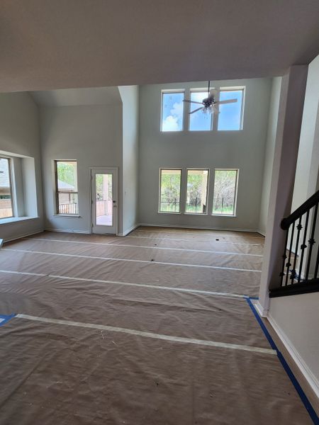 A spacious living room with high ceilings, large windows, and a ceiling fan, bathed in natural light.