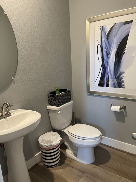 A modern half-bath with a pedestal sink, sleek fixtures, and contemporary artwork on gray walls.