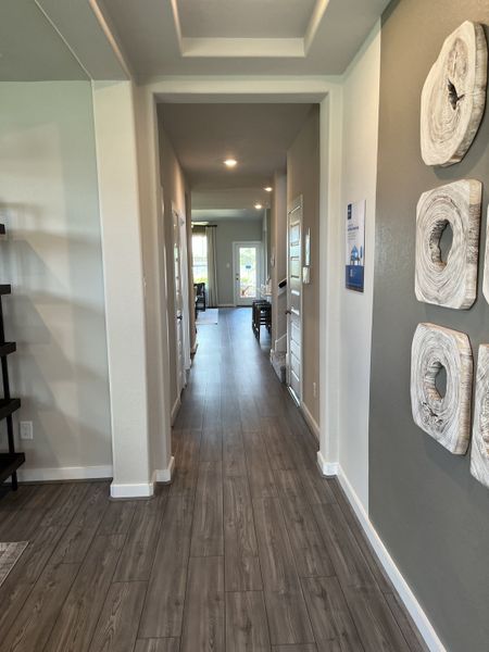 A modern hallway with gray wooden flooring, recessed lighting, and artistic wall decor leading to a bright living area.