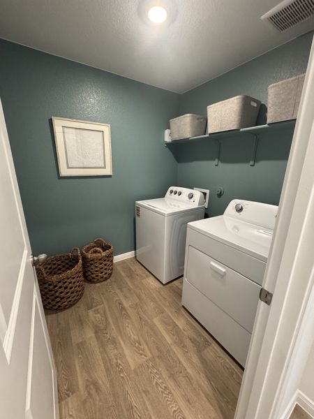 A cozy laundry room with teal walls, wood flooring, wicker baskets, and modern appliances. A cozy laundry room with teal walls, wood flooring, wicker baskets, and modern appliances.