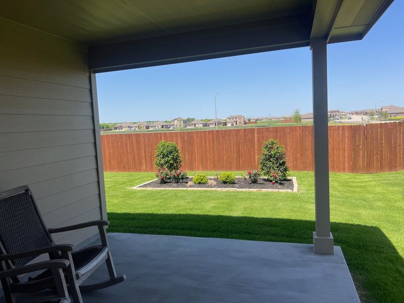 A cozy patio overlooks a lush green lawn and landscaped garden beds, framed by a wooden fence. A cozy patio overlooks a lush green lawn and landscaped garden beds, framed by a wooden fence.