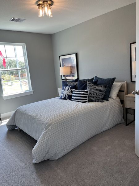 A cozy bedroom with soft gray walls, striped bedding, and decorative pillows under elegant ceiling lighting.