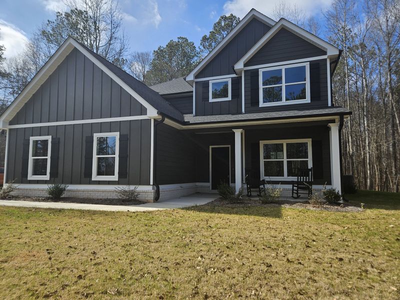 A modern farmhouse-style home exterior with dark siding, white trim, a covered porch, and rocking chairs.