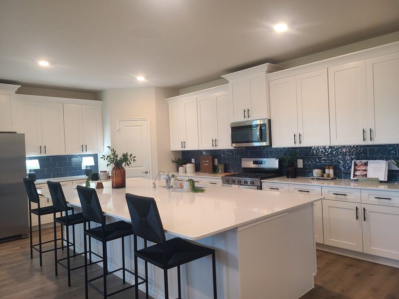 A modern kitchen with crisp white cabinets, sleek blue tile backsplash, and a spacious island with seating.