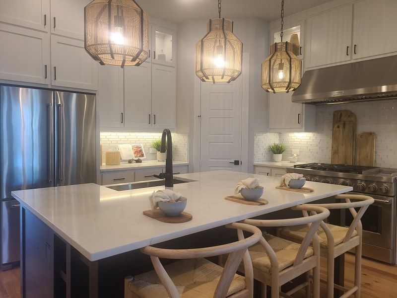 A modern kitchen with pendant lighting, white cabinetry, stainless appliances, and a spacious island with wood stools. A modern kitchen with pendant lighting, white cabinetry, stainless appliances, and a spacious island with wood stools.