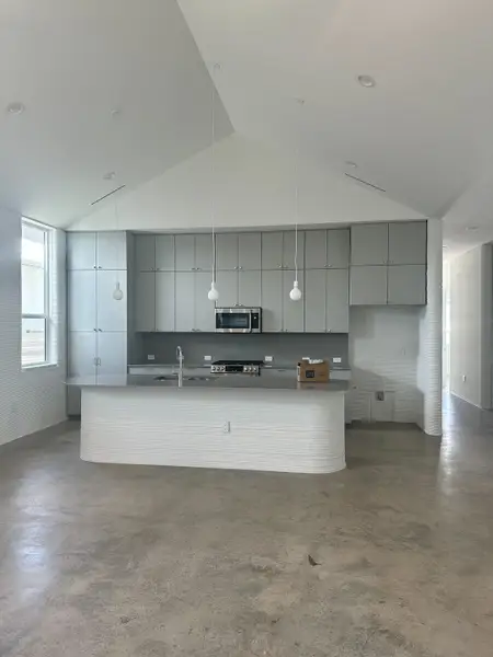 A modern kitchen with sleek grey cabinetry, concrete floors, and pendant lighting over a curved island.