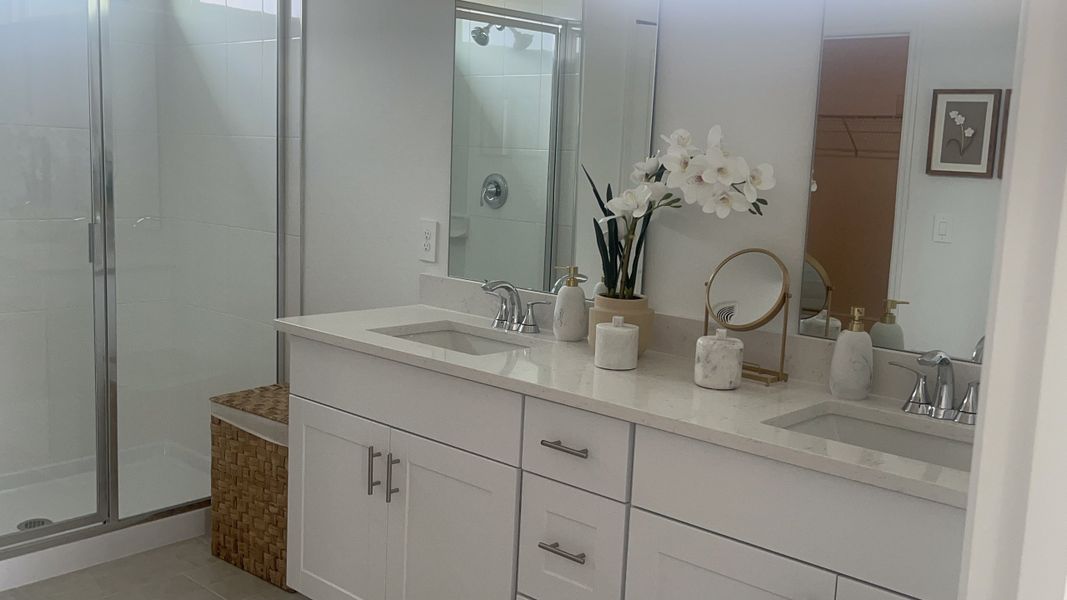 A sleek bathroom with a double vanity, modern fittings, and elegant decor, featuring a glass-enclosed shower and chic accessories.