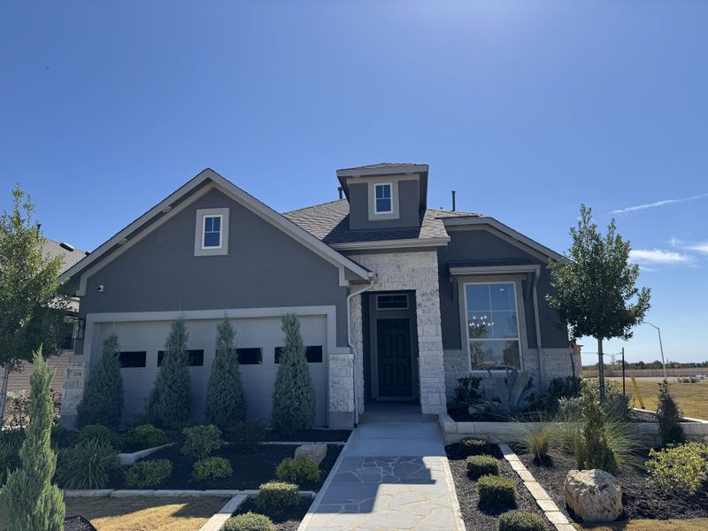 A charming gray home with a stone façade and landscaped yard in Nolina by Chesmar Homes (Georgetown, TX).