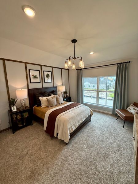 A cozy bedroom with a modern chandelier, stylish artwork, and a large window offering natural light. A cozy bedroom with a modern chandelier, stylish artwork, and a large window offering natural light.