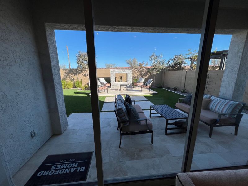 A cozy patio with stylish seating and a modern outdoor fireplace, offering a serene view of a landscaped garden.