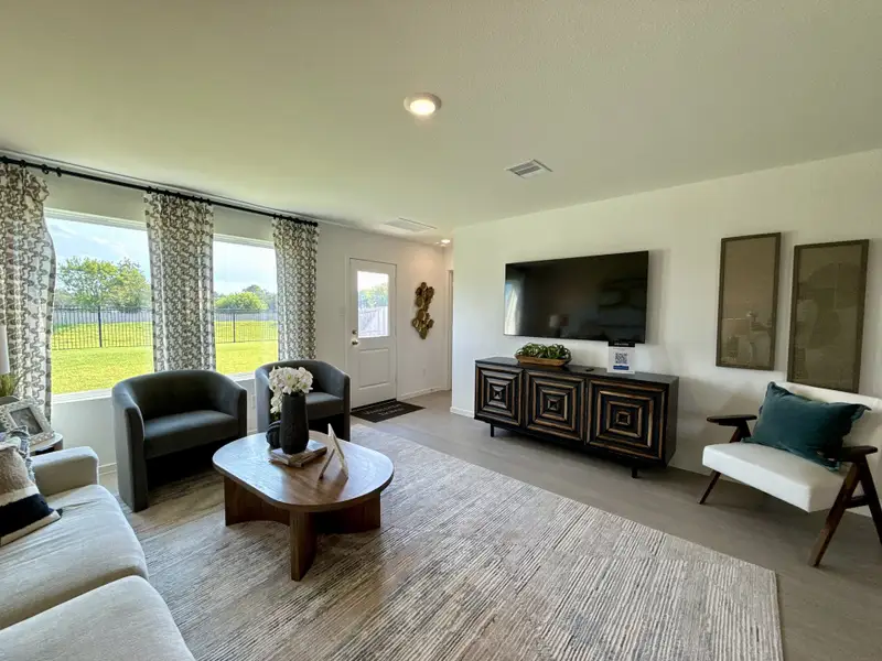 A cozy living room with patterned curtains, sleek furniture, a modern TV setup, and a view of the spacious backyard.