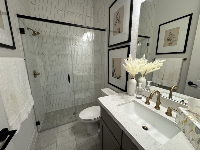 A sleek bathroom with a hexagonal-tiled shower, elegant gold fixtures, and decorative framed art. A sleek bathroom with a hexagonal-tiled shower, elegant gold fixtures, and decorative framed art.