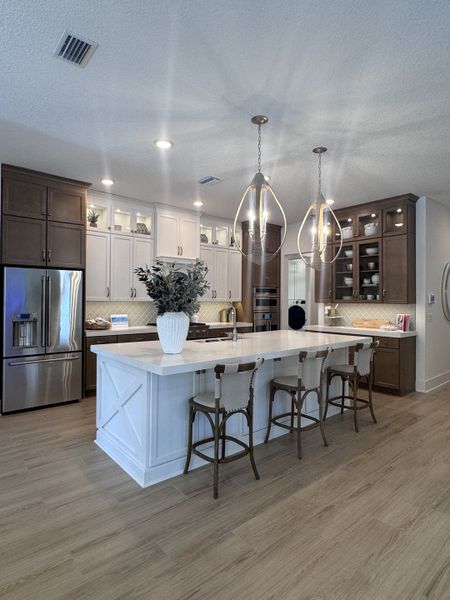 A modern kitchen with a large island, elegant pendant lights, wood cabinets, and sleek stainless appliances.