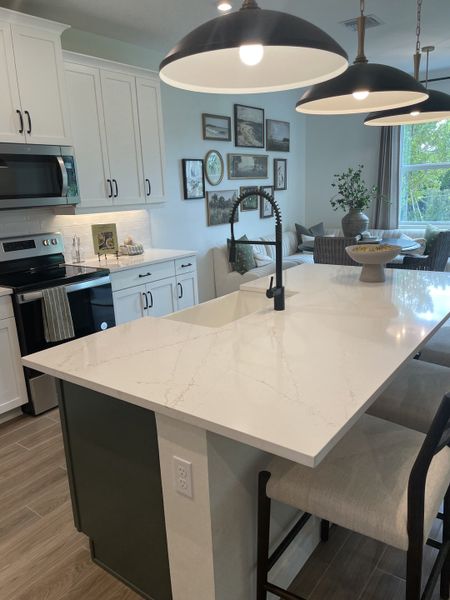 A modern kitchen with white cabinetry, a sleek island, artistic lighting, and a cozy dining area.
