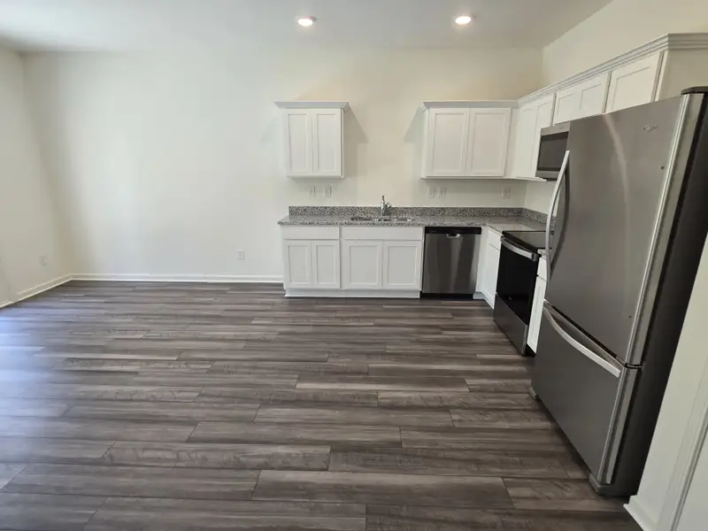 A sleek kitchen with wood flooring, white cabinets, stainless steel appliances, and granite countertops.