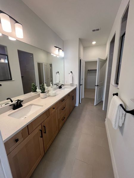 A modern bathroom with a long wooden vanity, dual sinks, and sleek black fixtures.