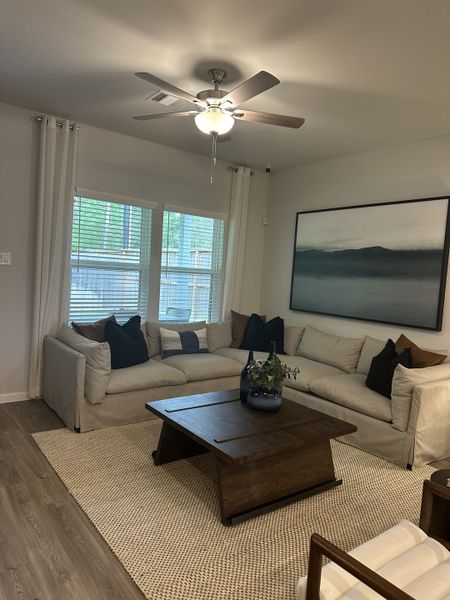 A cozy living room with a plush sectional sofa, chic wooden coffee table, and modern ceiling fan. Neutral tones create a serene vibe.