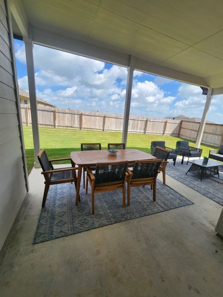 A cozy covered patio with elegant outdoor furniture and a serene view of the expansive fenced backyard. A cozy covered patio with elegant outdoor furniture and a serene view of the expansive fenced backyard.