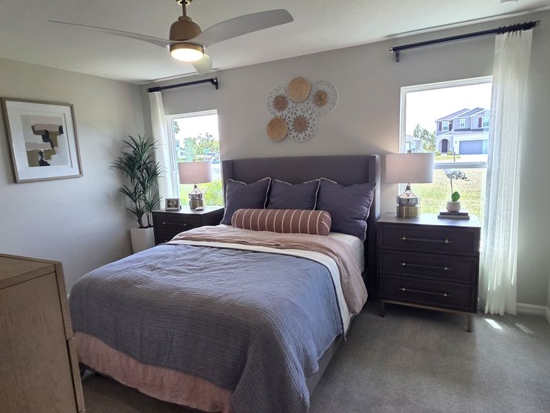 A cozy bedroom with a plush bed, modern ceiling fan, and elegant decor, featuring large windows and stylish furniture.