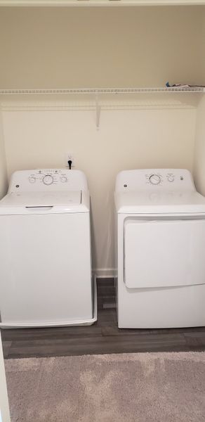 A convenient laundry room with modern white washer and dryer, featuring ample shelving and a cozy carpeted floor. A convenient laundry room with modern white washer and dryer, featuring ample shelving and a cozy carpeted floor.