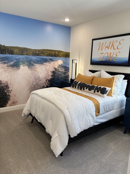 A cozy bedroom featuring a bold mural of a lake view and stylish "Wake Zone" decor above a plush bed.