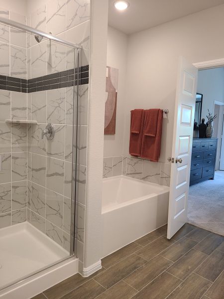 A contemporary bathroom featuring a marble-tiled shower, inviting bathtub, and warm wood flooring.