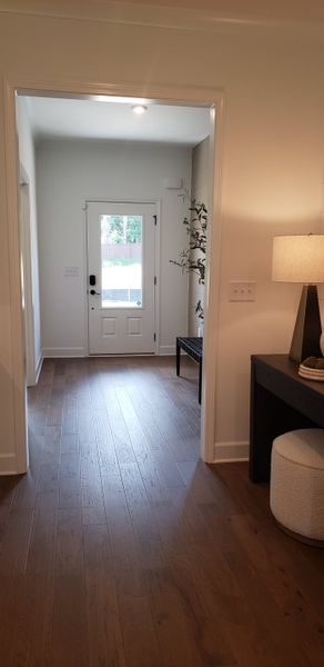 A welcoming entryway with warm wood flooring, bright white walls, a stylish bench, and soft lamp lighting.