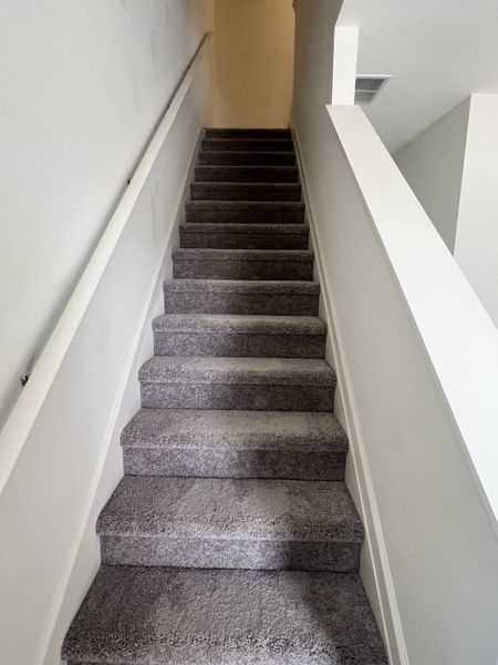 A carpeted staircase with sleek white walls, providing a cozy and modern ascent to the upper level.