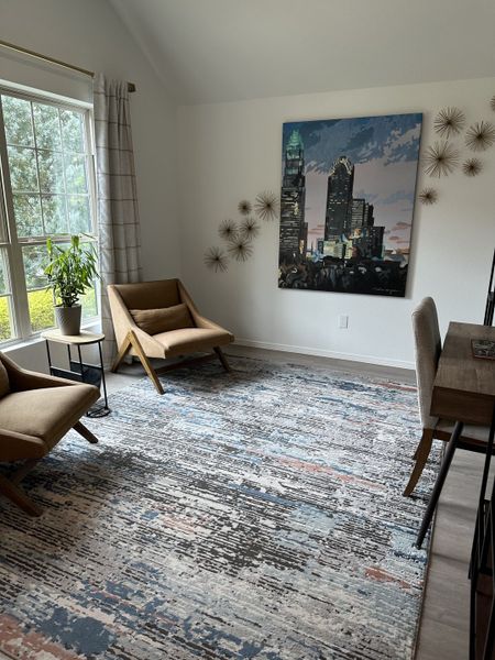 A cozy room with chic chairs, artistic decor, and a large window, featuring a patterned area rug and urban artwork. A cozy room with chic chairs, artistic decor, and a large window, featuring a patterned area rug and urban artwork.