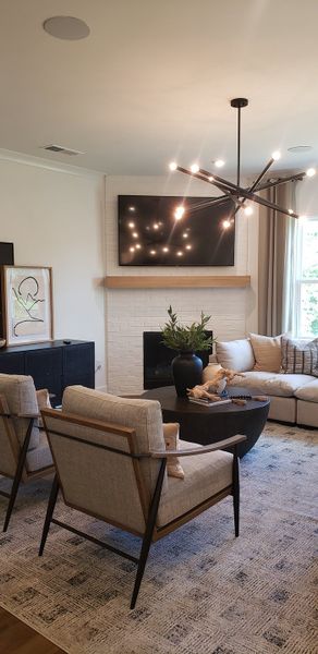 A cozy living room featuring a modern chandelier, plush seating, and a brick fireplace with mounted TV.