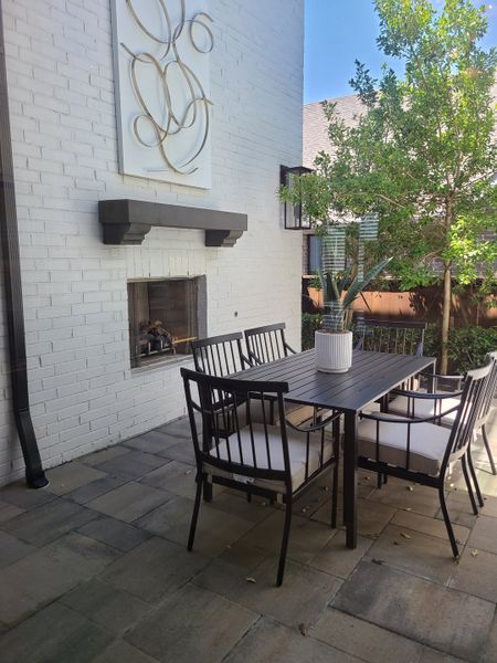 A chic outdoor patio featuring a modern fireplace, metal dining set, and serene greenery for stylish relaxation. A chic outdoor patio featuring a modern fireplace, metal dining set, and serene greenery for stylish relaxation.