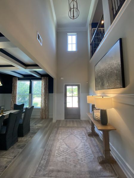 A bright entryway featuring a tall ceiling, elegant lighting, and a chic rug, leading into a formal dining area.