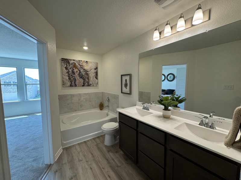 A modern bathroom featuring dual sinks, a sleek tub, and bright lighting with natural light from an adjacent room. A modern bathroom featuring dual sinks, a sleek tub, and bright lighting with natural light from an adjacent room.