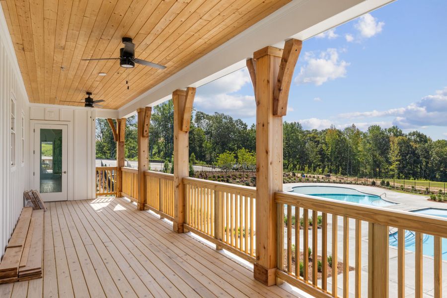 A deck with a pool and a wood railing with trees in the background.