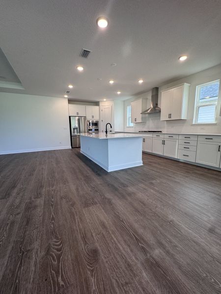 A modern kitchen with sleek white cabinetry, a spacious island, and elegant lighting on warm wood flooring.