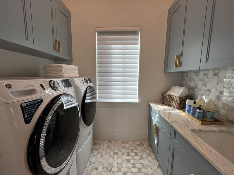A modern laundry room featuring sleek gray cabinets, a marble countertop, and high-efficiency washer and dryer units.