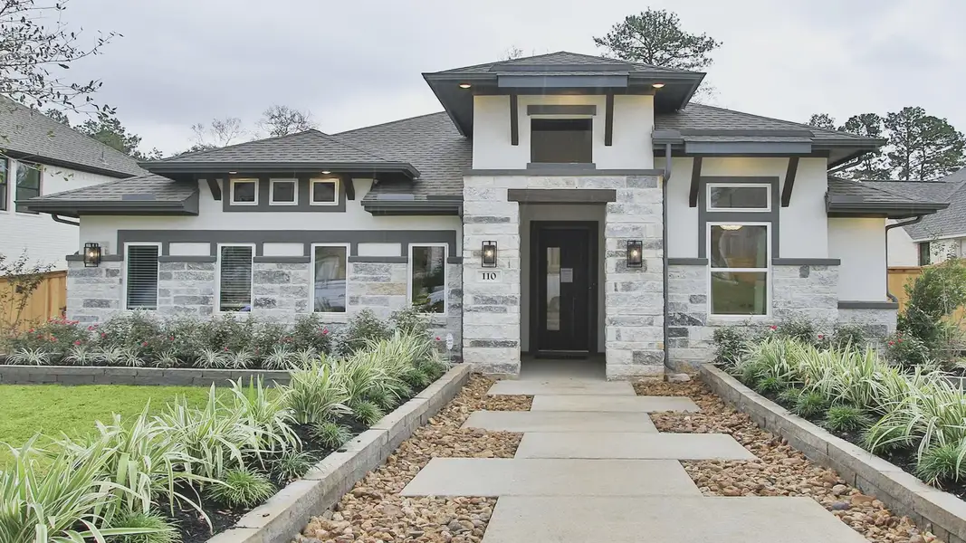 Exquisite stone facade with chic black accents, nestled in lush landscape. The Woodlands Hills.