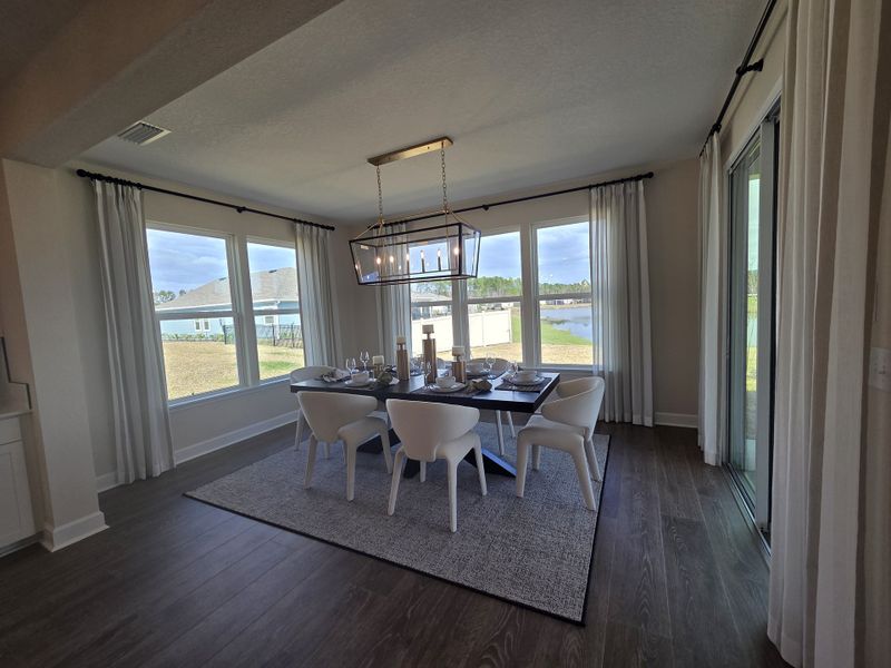 A bright dining room with large windows, elegant chairs, a rectangular table, and a stylish chandelier overlooking a serene view.