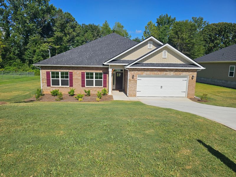 A beautiful brick home with vibrant shutters and a lush lawn in Scarlett Place by Adams Homes (Bowdon, GA).